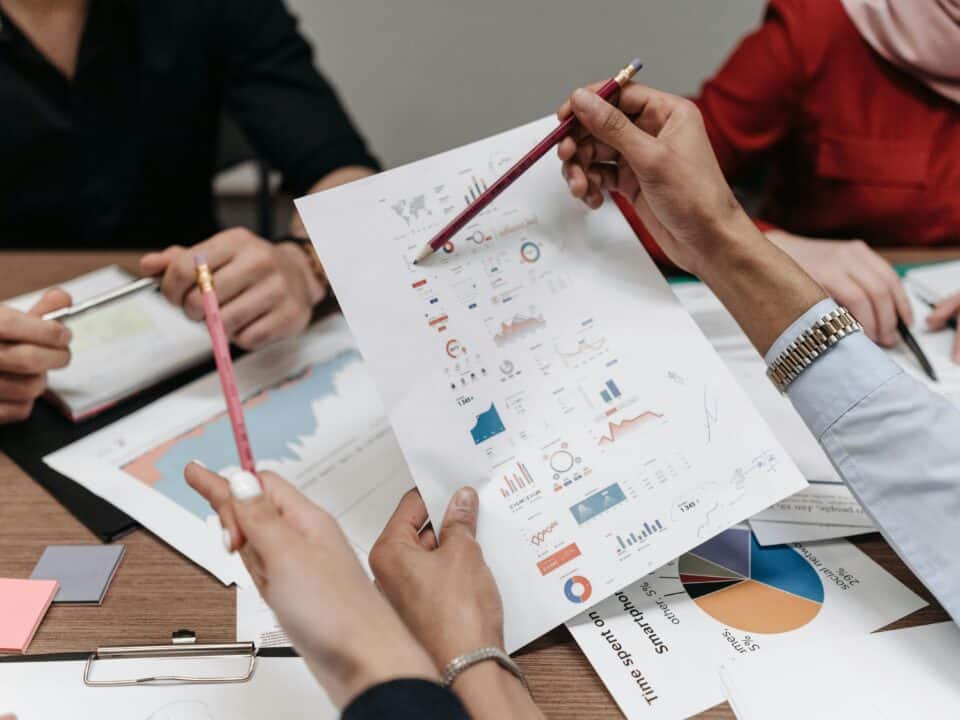 Il s'agit d'une image montrant 3 personnes en réunion stratégique pour leurs entreprise. Les 3 personnes sont avec des feuilles montrant des données de la situation de l'entreprise. Et discute surement d'une stratégie à adopter.